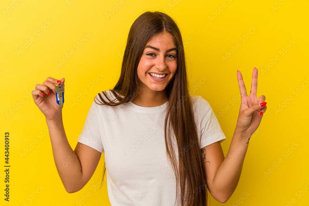 Young caucasian woman holding a home keys isolated on yellow background showing number two with fingers.