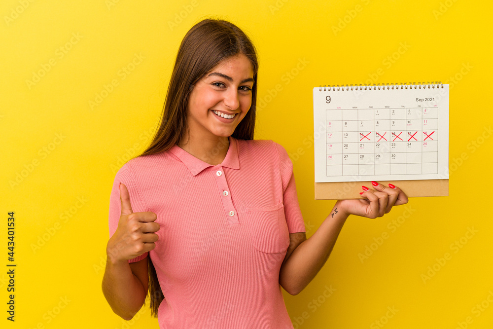 Young caucasian woman holding a calendar isolated on yellow background smiling and raising thumb up Young caucasian woman holding a calendar isolated on yellow background smiling and raising thumb up