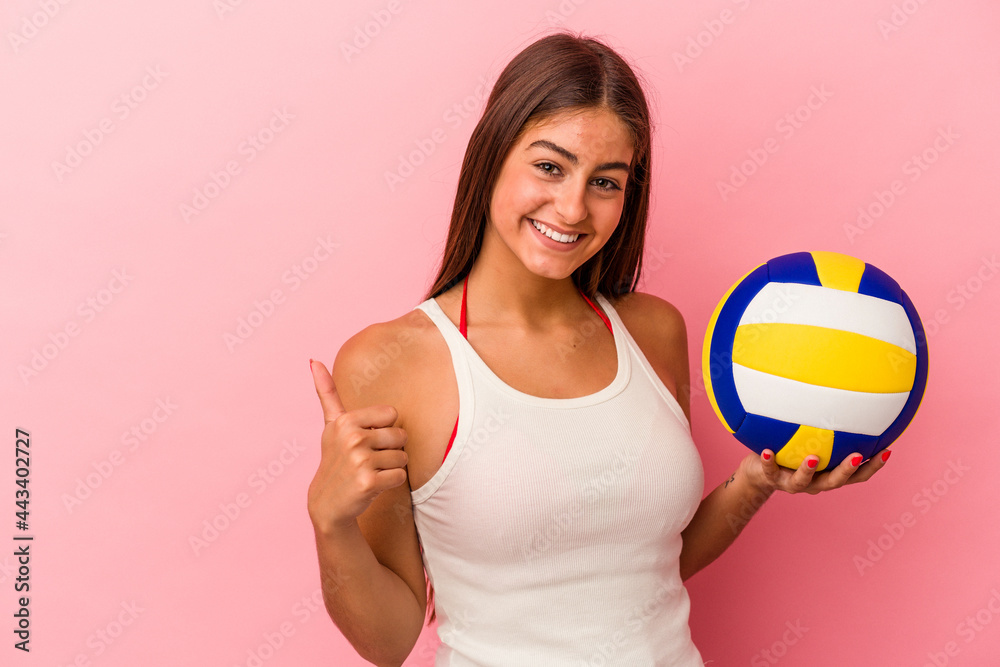 Young caucasian woman holding a volleyball ball isolated on pink background smiling and raising thumb up