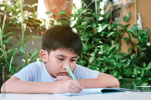 Asian boy doing his homework using a pen to write on a notebook.