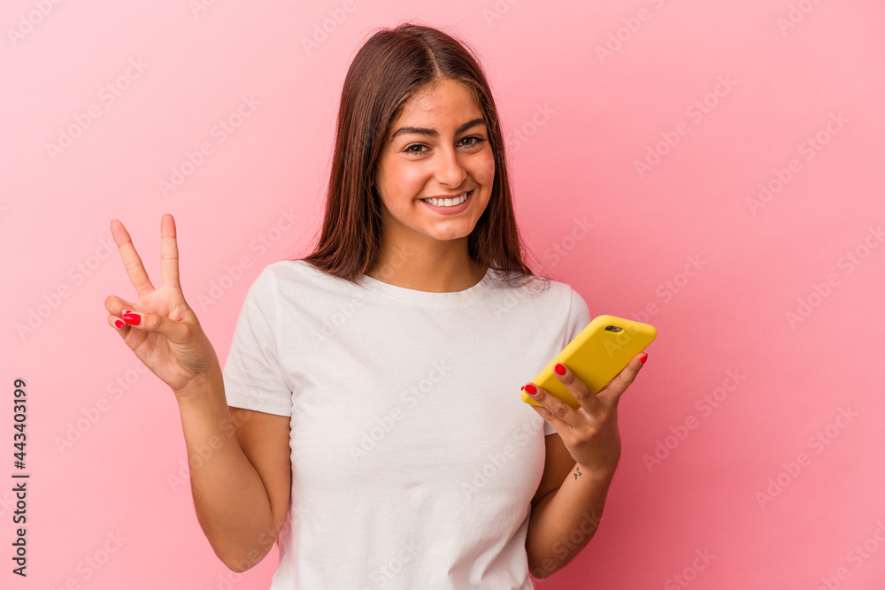 Young caucasian woman holding a mobile phone isolated on pink background showing number two with fingers. Young caucasian woman holding a mobile phone isolated on pink background showing number two with fingers.