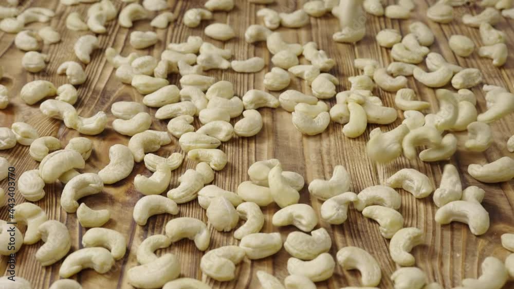 Raw cashew lying on a textured wooden table surface. Peeled white kernels fall onto the table. Organic healthy food background. Close up. Slow motion. Raw cashew lying on a textured wooden table surface. Peeled white kernels fall onto the table. Organic healthy food background. Close up. Slow motion.