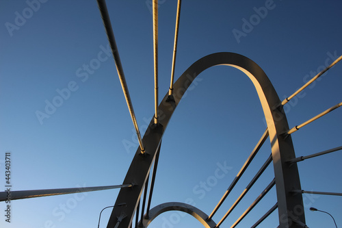 Bottom view of the cable-stayed bridge pylon and cables with red sunset reflections on the metal of the structures  © Elena