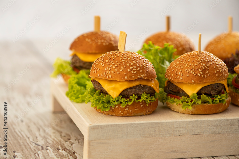 mini burgers with cheese and lettuce with sticks on a wooden background - obrazy, fototapety, plakaty 