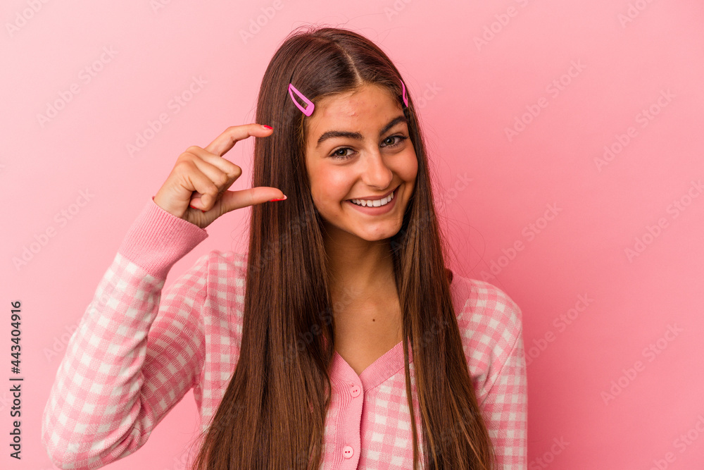 Fototapeta premium Young caucasian woman isolated on pink background holding something little with forefingers, smiling and confident.