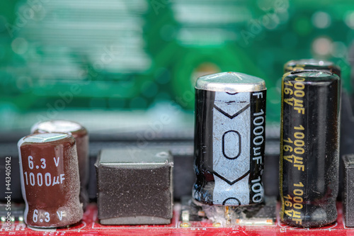 Damaged capacitor on a circuit board. Top is bulged out showing failure. Undamaged capacitors also present. No brand markings. Shallow depth of field.