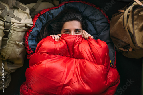 A young woman in a comfortable sleeping bag in a tent, top view. A tourist in a sleeping bag. A traveler wrapped in a red sleeping bag. Travel, camping concept, adventure. Traveling with a tent photo