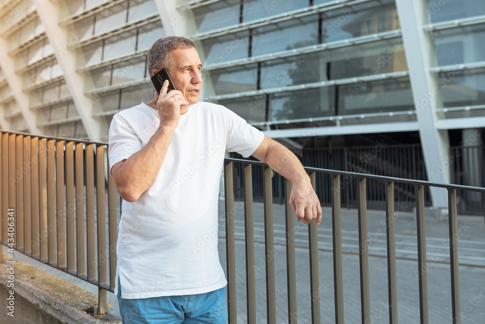 A man in a sports T-shirt and shorts speaks on the phone against a blurred background of the stadium. Sunlight. Evening run. A minute of rest from the sports back. solving business issues