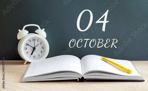 october 04. 04-th day of the month, calendar date.A white alarm clock, an open notebook with blank pages, and a yellow pencil lie on the table.Autumn month, day of the year concept