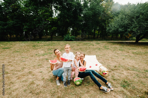 Boy, girls with mother eating watermelon in the summer. Happy family in the park on holidays.