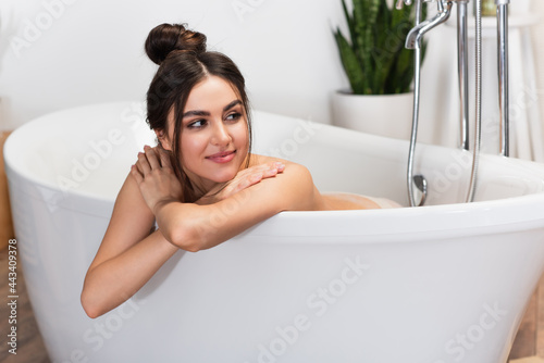 happy young woman with hair bun looking away while taking bath