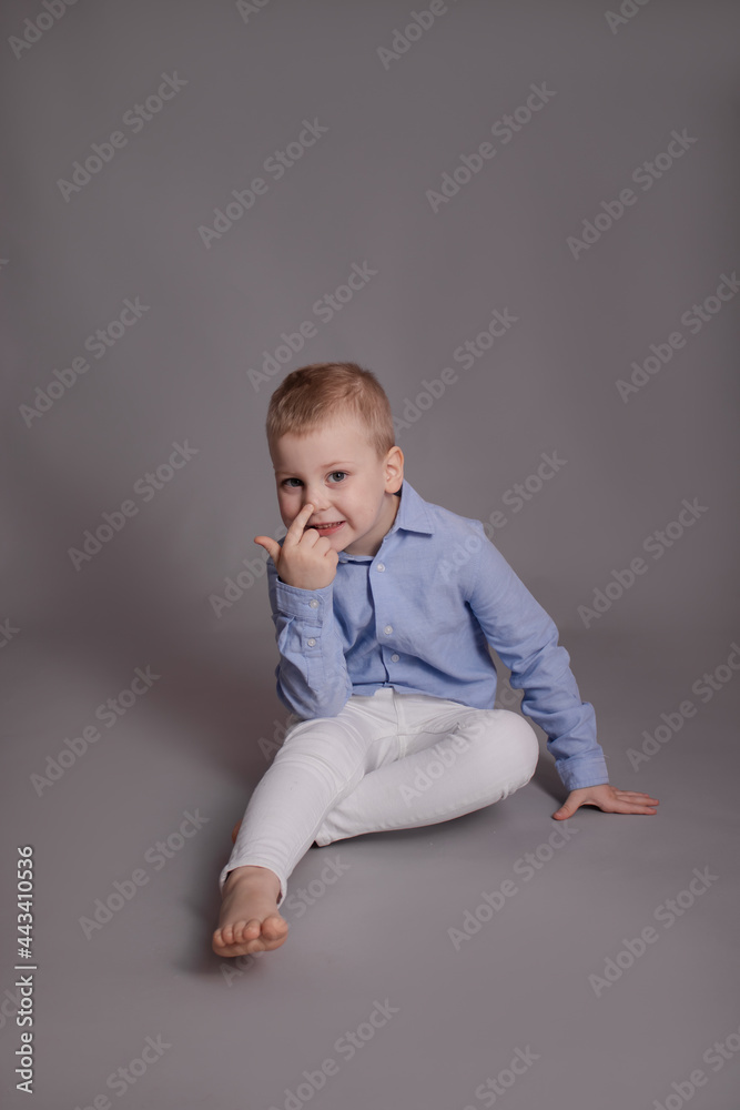 preschool blonde boy in white pants and blue shirt on grey background. child, kid isolated preschool blonde boy in white pants and blue shirt on grey background. child, kid isolated
