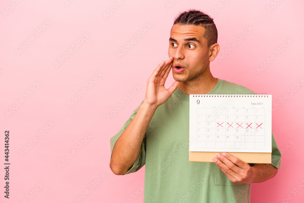 Young venezuelan man holding a calendar isolated on pink background is saying a secret hot braking news and looking aside Young venezuelan man holding a calendar isolated on pink background is saying a secret hot braking news and looking aside