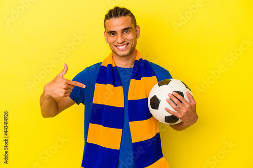 Young venezuelan man watching soccer isolated on yellow background person pointing by hand to a shirt copy space, proud and confident