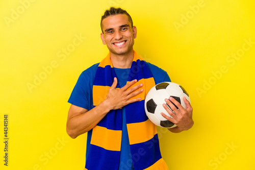 Young venezuelan man watching soccer isolated on yellow background laughs out loudly keeping hand on chest.