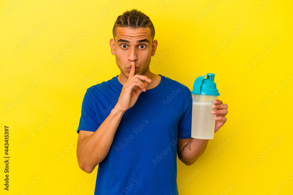 Young venezuelan man drinking a protein shake isolated on yellow background keeping a secret or asking for silence. Young venezuelan man drinking a protein shake isolated on yellow background keeping a secret or asking for silence.