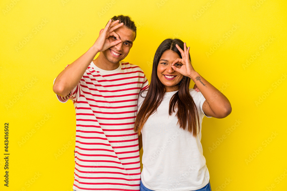 Young latin couple isolated on yellow background excited keeping ok gesture on eye. Young latin couple isolated on yellow background excited keeping ok gesture on eye.