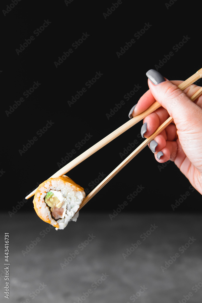 One piece of sushi in chopsticks, isolated on black background. Japanese cuisine concept, copy space banner. One piece of sushi in chopsticks, isolated on black background. Japanese cuisine concept, copy space banner.