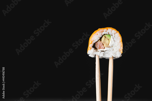 One piece of sushi in chopsticks, isolated on black background. Japanese cuisine concept, copy space banner.