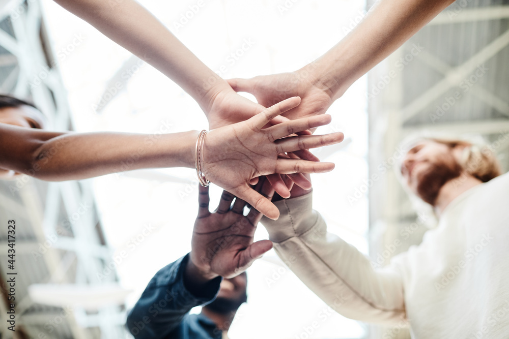 Low angle close up of multi-ethnic group of young people stacking hands outdoors and celebrating friendship Low angle close up of multi-ethnic group of young people stacking hands outdoors and celebrating friendship