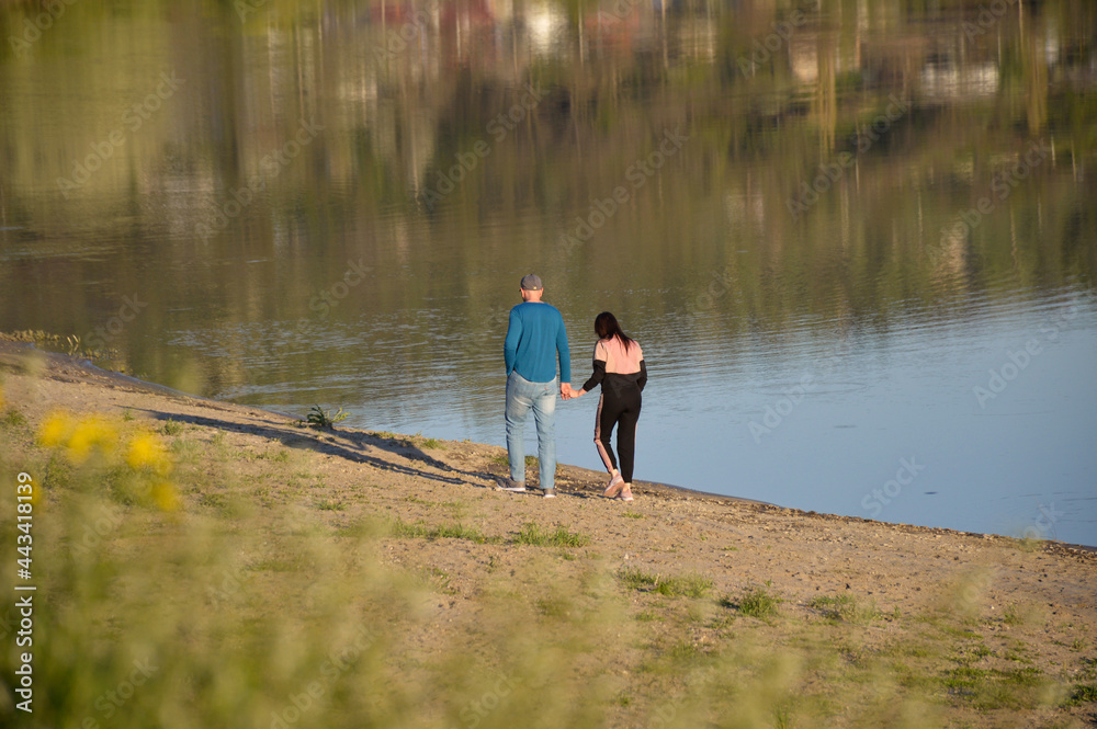 a couple in love, a man and a woman walk along the shore of a reservoir at sunset and hold hands