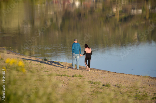 a couple in love, a man and a woman walk along the shore of a reservoir at sunset and hold hands