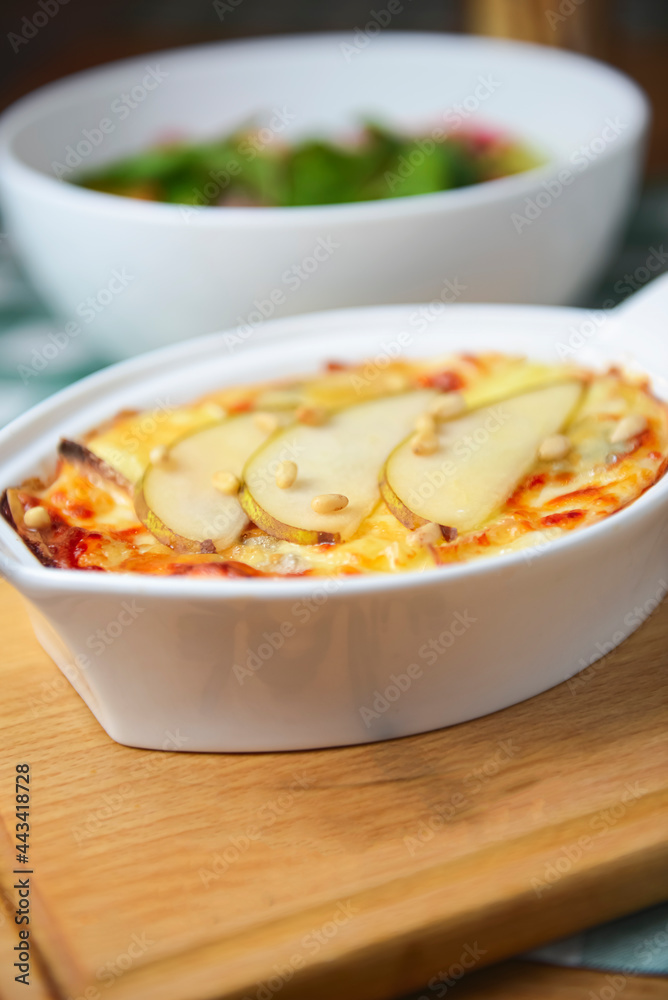 Cottage cheese and potato casserole with pears served in a white casserole dish and vegetable salad on the background.