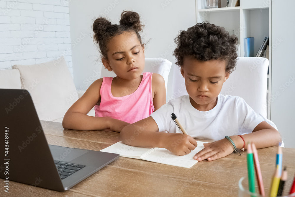 African american elder sister watching younger brother doing homework at desk African american elder sister watching younger brother doing homework at desk