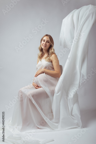 Elegant pregnant young woman standing wearing flying white fabric. Pregnancy, maternity and motherhood concept.