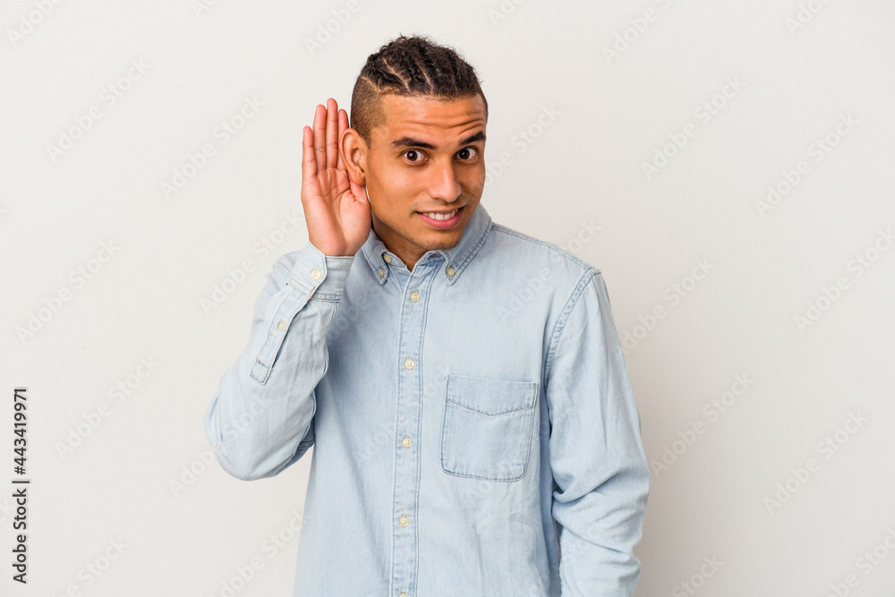 Young venezuelan man isolated on white background trying to listening a gossip. Young venezuelan man isolated on white background trying to listening a gossip.