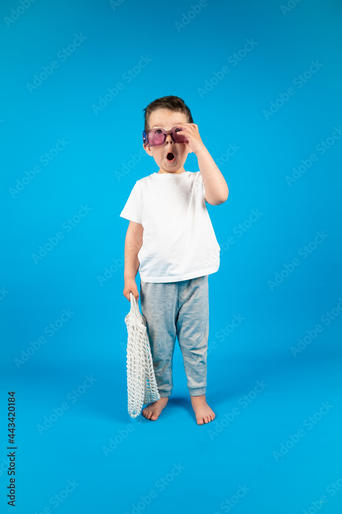 Surprised little boy puts on violet sunglasses and holds mesh shopping bag in hand. Discounts and sales concept Surprised little boy puts on violet sunglasses and holds mesh shopping bag in hand. Discounts and sales concept