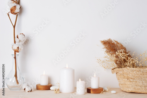 Home decoration with candles  basket and flowers over white wall. Interior design concept. Close up  copy space