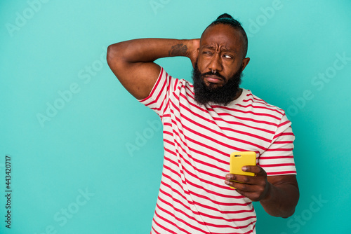 African american man holding a mobile phone isolated on blue background touching back of head, thinking and making a choice.