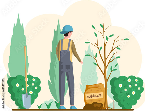 Man with shovel standing near tree in garden. Guy buries seedling in ground for planting trees. Professional gardener worker applies fertilizers to pit. Farmer works in field. Spring farm work in yard