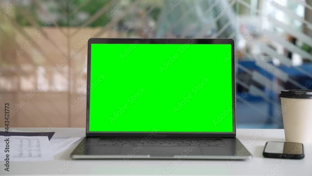 Workplace with laptop computer on desk with blank empty green mockup screen for advertising standing in modern contemporary office. Business software website ads technology concept.
