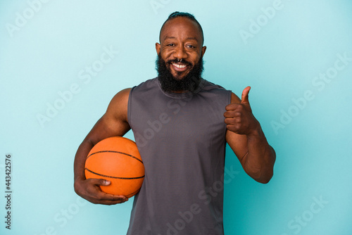 African american man playing basketball isolated on blue background smiling and raising thumb up © Asier