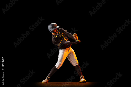 Professional baseball player, pitcher in sports uniform and equipment playing baseball isolated on black studio background in neon light. Team sport concept © master1305
