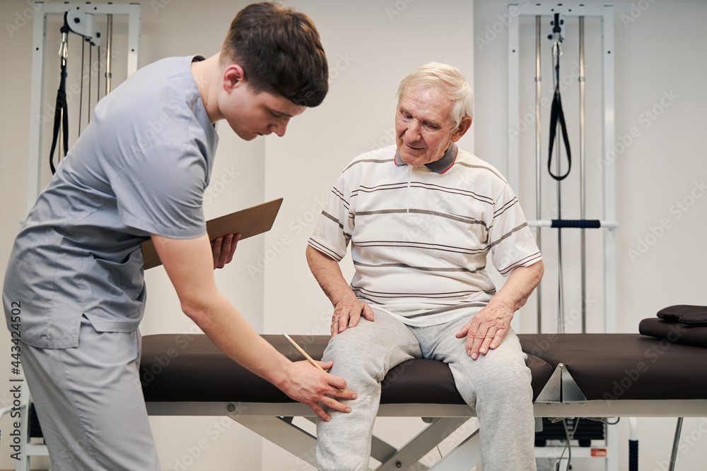 Manual therapist touching aching knee of elderly person Manual therapist touching aching knee of elderly person
