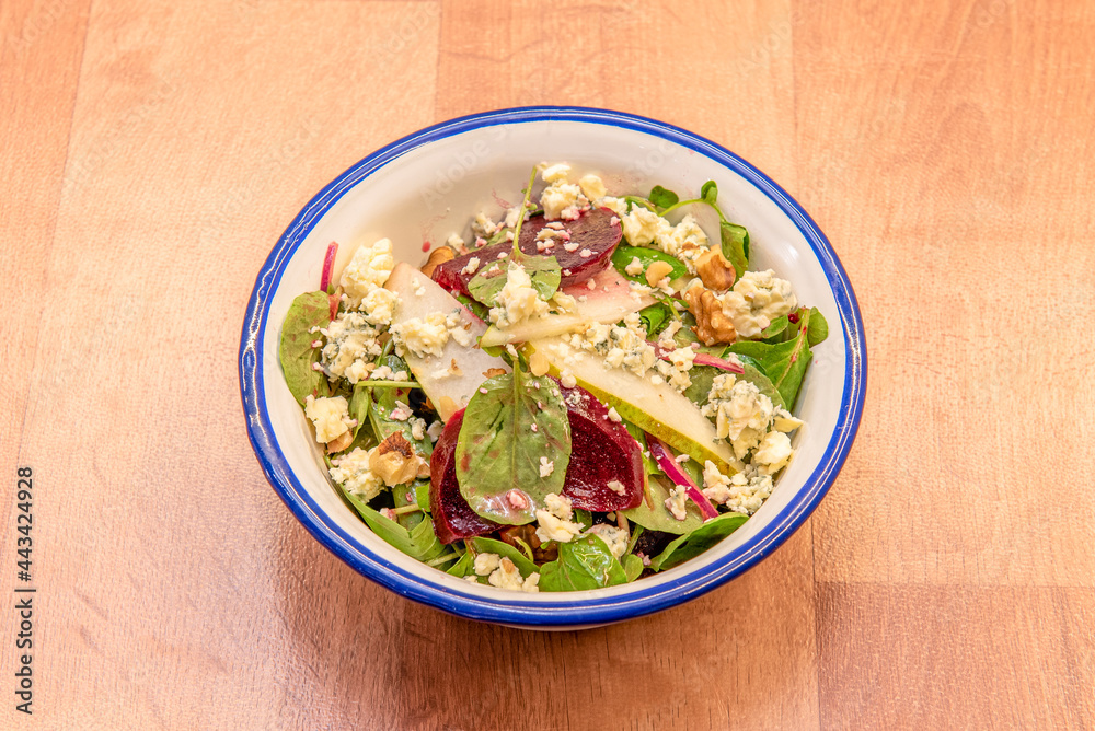 Spinach salad with beetroot slices, pear thin slices, crumbled blue cheese, pieces of nuts inside an enameled metal bowl
