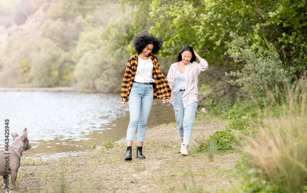 Cheerful multiethnic couple of lesbian women walking in forest