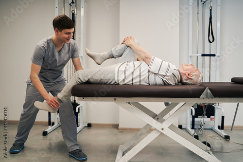 Pensioner stretching right leg while doctor pulling his left one