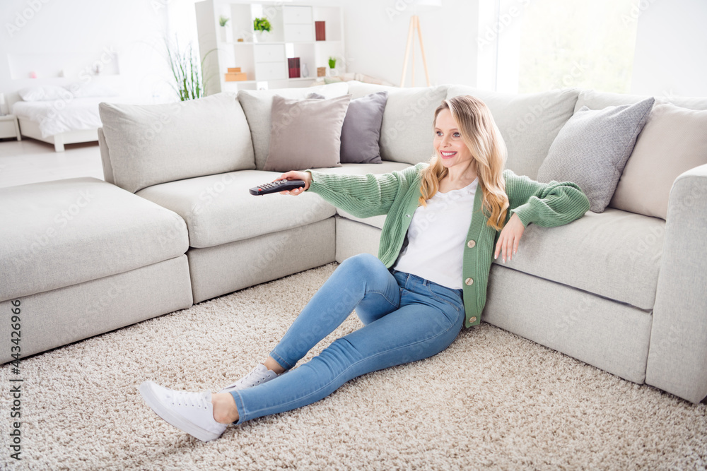 Portrait of attractive cheerful wavy-haired girl sitting on floor resting free time watching show series at home light white flat indoors Portrait of attractive cheerful wavy-haired girl sitting on floor resting free time watching show series at home light white flat indoors
