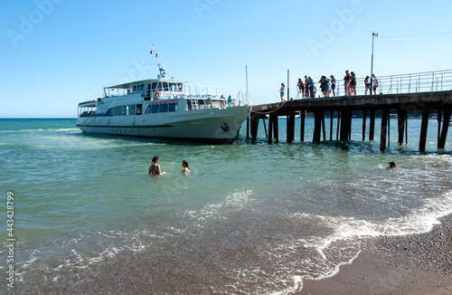 The green Sea, a white steamer is standing at the old pier. Passengers are waiting for boarding. Girls swim in the surf. Gurzuf, Yalta, Crimea.