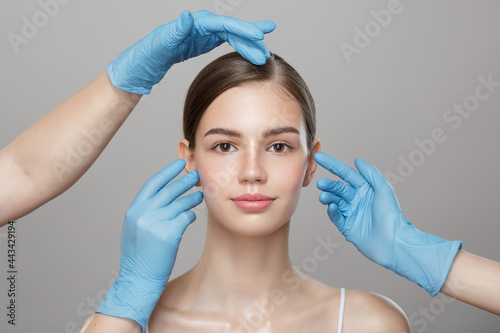 People, cosmetology, plastic surgery and beauty concept - surgeon or beautician hands touching woman face over gray background.