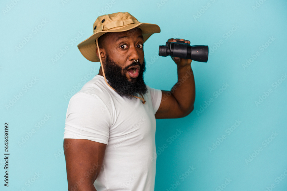 African american man holding binoculars isolated on blue background African american man holding binoculars isolated on blue background