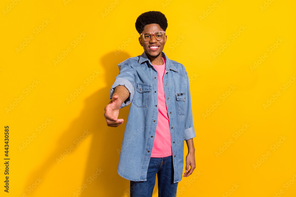 Photo of happy positive dark skin man good mood smile wear glasses handshake isolated on yellow color background Photo of happy positive dark skin man good mood smile wear glasses handshake isolated on yellow color background