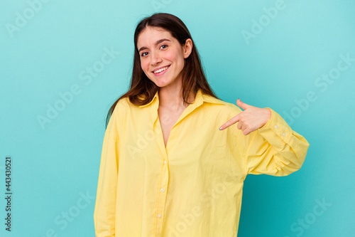 Young caucasian woman isolated on blue background person pointing by hand to a shirt copy space, proud and confident