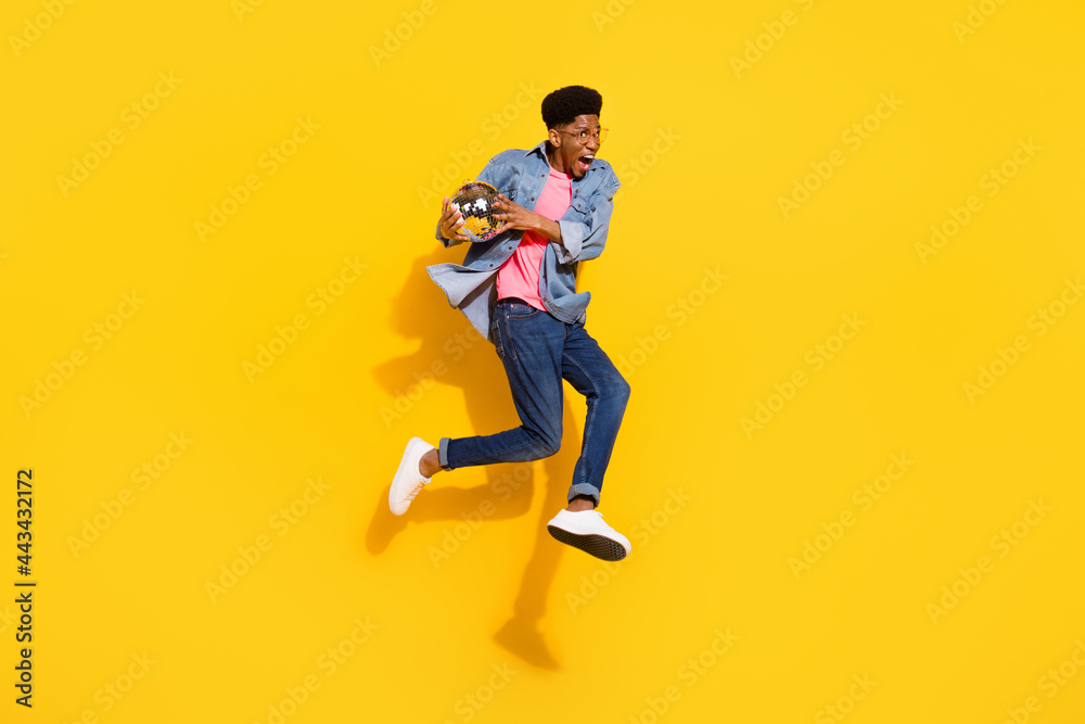 Full size photo happy cheerful dark skin man jump up hold disco ball enjoy isolated on yellow color background