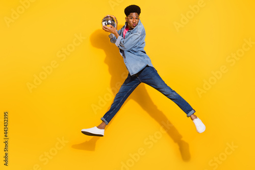 Full size photo of afro american man jump wear denim jeans shirt hold disco ball send air kiss isolated on yellow color background © deagreez