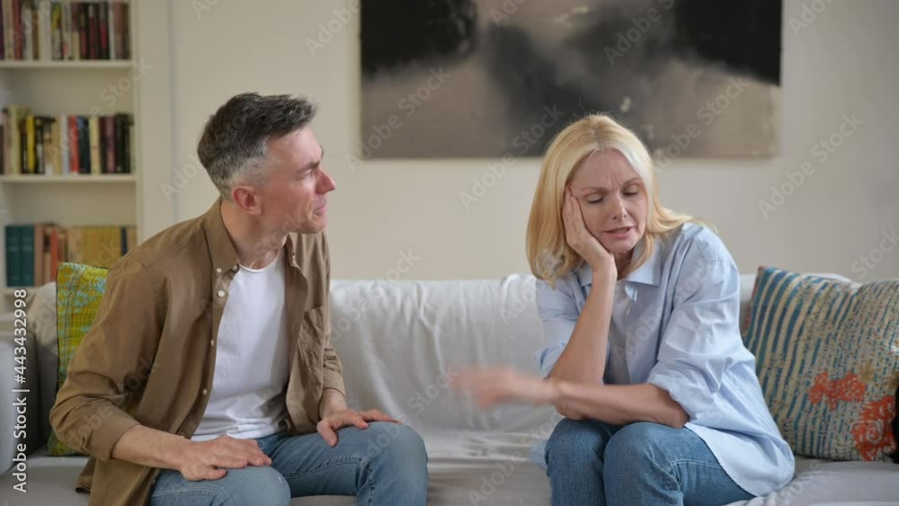 Misunderstanding, family quarrel. Upset, indignant gray-haired husband is emotionally talking and looking at his wife, gesturing with his hands, wife is upset because of a dialog, experiencing stress Misunderstanding, family quarrel. Upset, indignant gray-haired husband is emotionally talking and looking at his wife, gesturing with his hands, wife is upset because of a dialog, experiencing stress